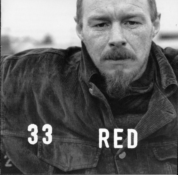 La pochette de l'album "33" de Red : une photo en noir en blanc d'un homme portant le bouc et une moustache, vêtu d'une chemise sombre. L'homme regarde l'appareil photo. La photo est cadrée sur son torse.L'arrière planc est flou, mais il est clair et la photo semble avoir été prise en extérieur.
Par dessus, en blanc, les mots "33" et "Red"