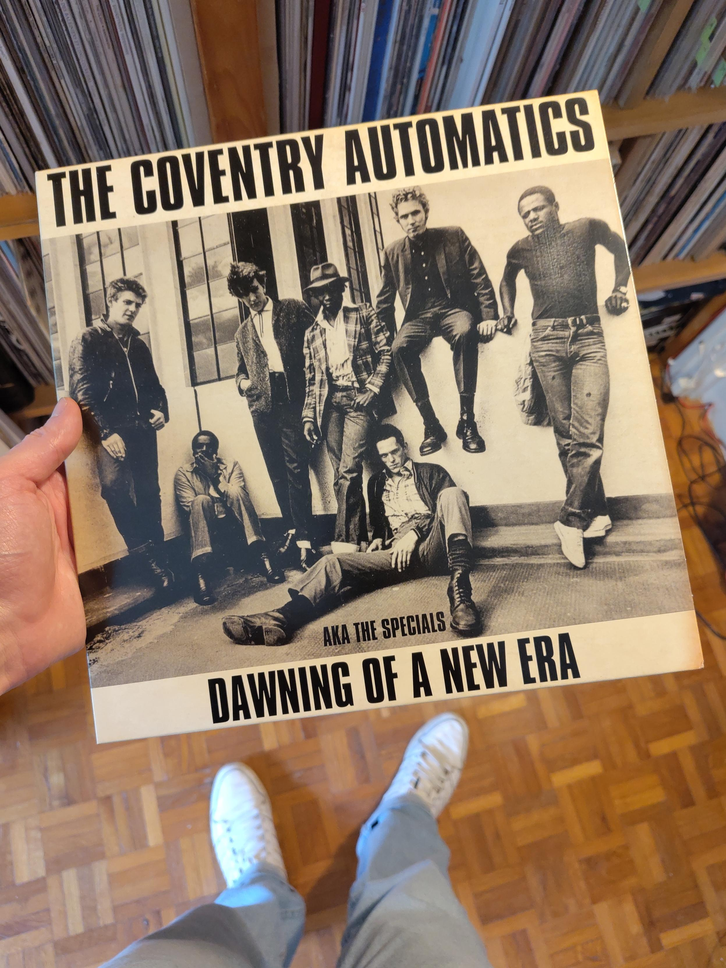 Sept hommes, noirs et blancs, habillées en rude boys et en skinhead, assis ou appuyés contre un muret, deux d'entre eux assis par terre. Ce sont les membres du groupe Coventry Automatics, bientôt mondialement connus avec le même répertoire sous le nom de Specials et créateurs du son two-tone.