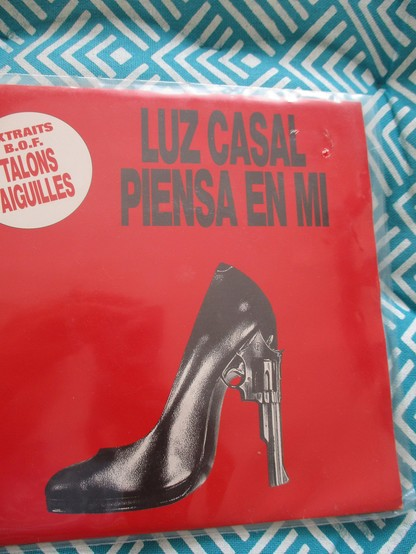 45T de Luz Casal pour "Piensa en mi" issu de la BO de Talons aiguilles d'Almodovar. La pochette est rouge sang, avec un talon haut noir dont l'aiguille est en fait un revolver