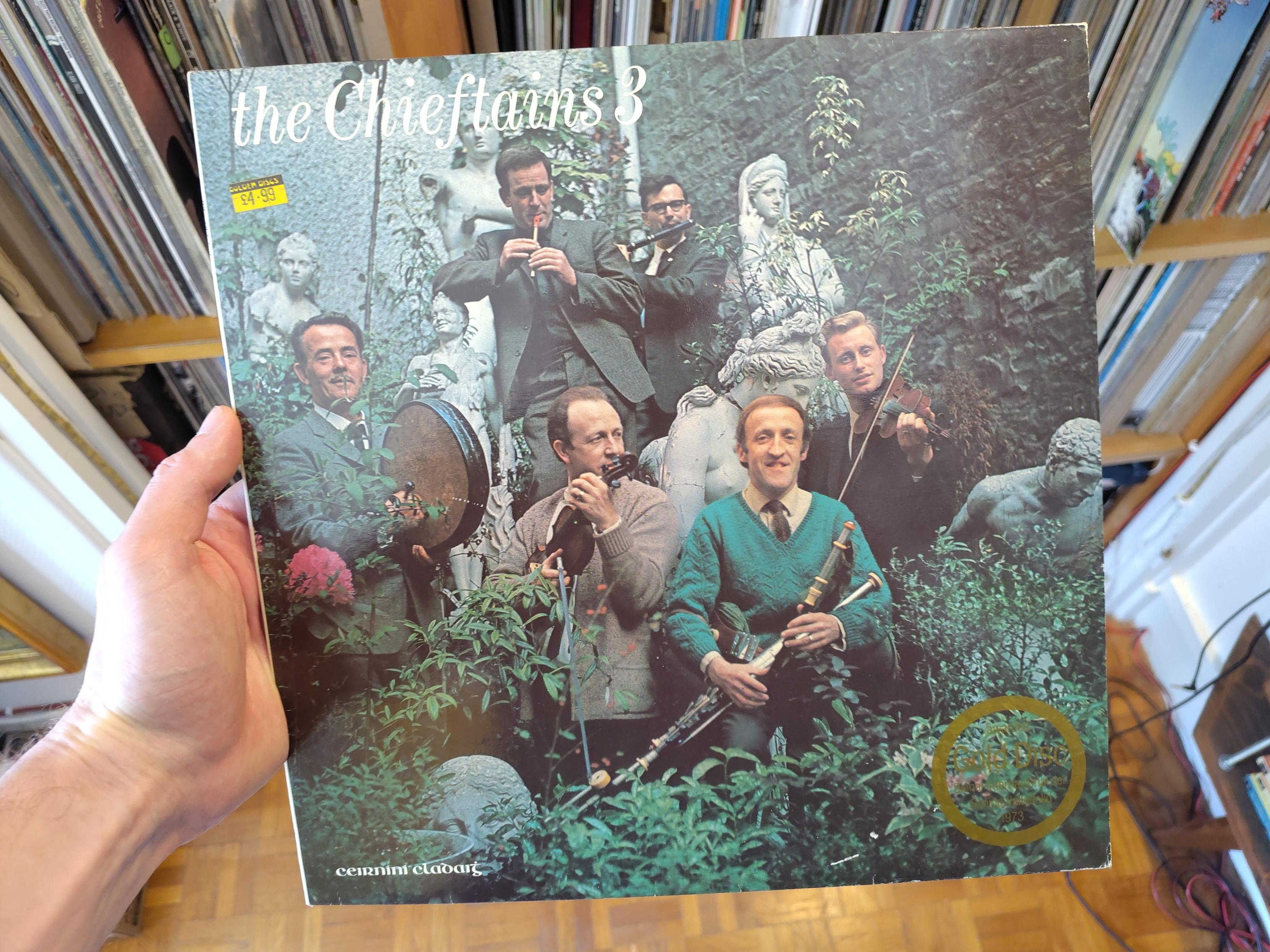 Le groupe avec ses instruments (flûte, tin whistle, bodhrán, violons et uilleann-pipe), pris en photo dans un jardin, au milieu de multiples statues antiques. Ils ont l'ai contents d'être là et détendus. Le joueur de tin whistle est négligemment accoudé sur la tête d'une statue et son air pince-sans-rire est celui de quelqu'un qui sait très bien ce qu'il fait et que ça le fait marrer.